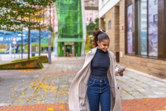 Happy young african american businesswoman using phone while walking on a rush along a city street