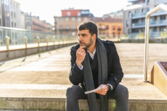 Casual businessman sitting pensive writing notes on notebook outdoors in the city in a sunny day of