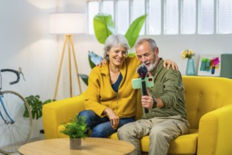 Senior couple taking selfie with smartphone sitting on a modern yellow sofa at home