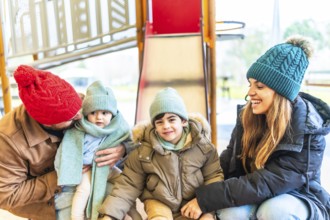 Smiling family with two children wearing winter clothes, hats and scarves enjoying time together on