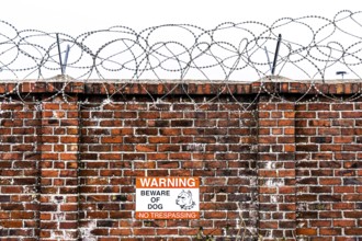 Company premises, wall secured with rolls of barbed wire, signpost for guard dog on the premises