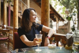 Cheerful and relaxed woman drinking white wine at rustic outdoor cafe enjoying tranquil ambiance of