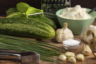 Fresh ingredients such as cucumbers, garlic, chives and sour cream on a wooden table with kitchen