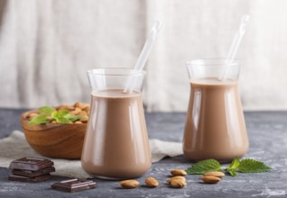 Organic non dairy almond chocolate milk in glass and wooden plate with almond nuts on a black