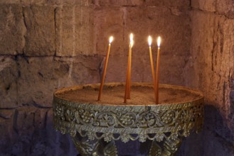 Several burning candles in an antique golden candlestick in front of a stone wall, creating a calm