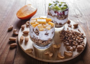 Dessert with greek yogurt, granola, almond, cashew, kiwi and persimmon on brown wooden background.