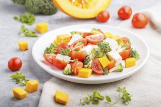 Vegetarian salad with broccoli, tomatoes, feta cheese, and pumpkin on white ceramic plate on a gray