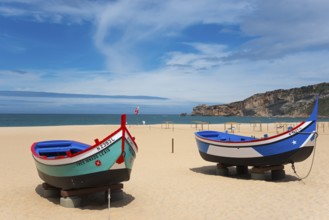 Two fishing boats on the sandy beach of Nazaré with a view of the sea and the cliffs, Praia da