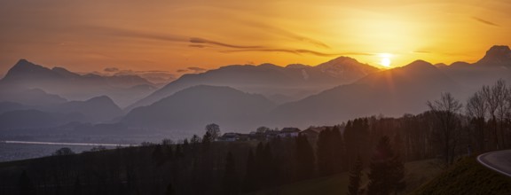 Sunset over a silhouetted mountain landscape, the sky glows in orange tones as dusk sets in,