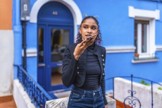African american woman sending a voice message with smartphone next to colorful blue house