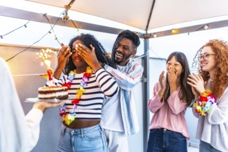African young woman with eyes covered receiving a birthday cake from multi-ethnic friends at