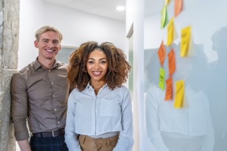 Two smiling coworkers standing in a coworking office near a whiteboard with colorful sticky notes