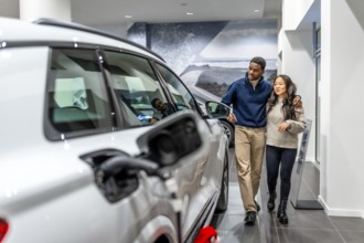 Multiethnic couple walking through a car dealership, happily selecting their new electric vehicle