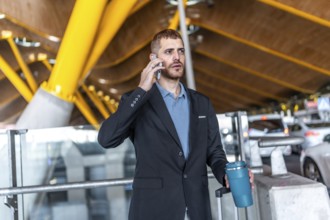 Businessman in a suit holding a reusable coffee cup while using a smartphone, waiting at the