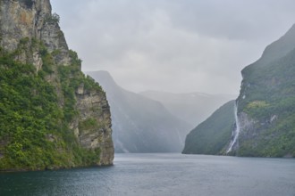 Geiranger Fjord with waterfall surrounded by rocks and mountains with overcast sky, Geiranger,