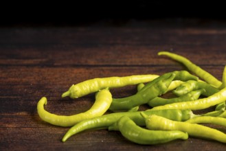 Several green peppers spread on a dark wooden surface, food photography