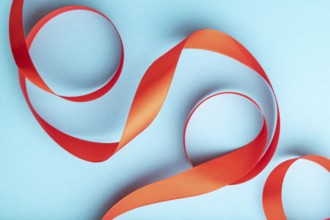Red coral ribbon on a blue pastel background. Celebration concept. Top view, close up, flat lay