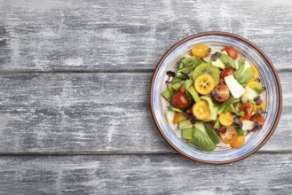 Vegetarian salad of pac choi cabbage, kiwi, tomatoes, kumquat, microgreen sprouts on gray wooden