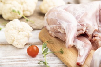 Whole raw rabbit with cauliflower, tomatoes and spices on a white wooden background and linen