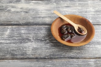 Pine cone jam in wooden bowl on gray wooden background. Side view, copy space