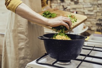 Unrecognizable man pours chopped green onions into a saucepan on a gas stove