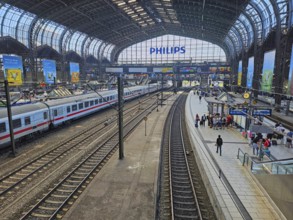 Hamburg central station with several tracks, an ICE train, under a vaulted steel roof, passengers
