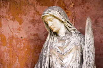 White angel with feather in front of red wall, angel statue, angel figure with peaceful face,
