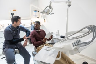 Dentist discussing treatment plan with patient using digital tablet in modern dental clinic,