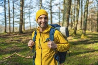 Hiker in a bright yellow jacket and backpack smiling while trekking through a sunlit forest,