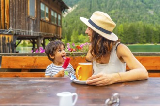 Mother and son enjoying a lakeside snack with a colorful popsicle and warm beverage against a