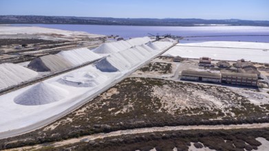 Aerial view of large salt cones forming alongside a pink lake and salt mine at sunset in