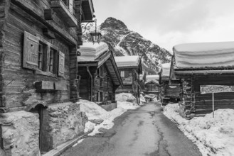 Street with historic old snow-covered wooden houses, black and white photo, mountain village Zinal,