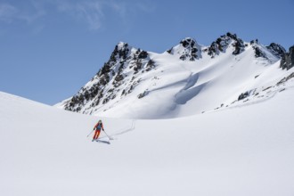 Ski tourer on the descent, minimalist winter landscape, white snow and dark mountains on the