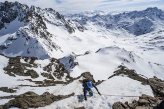 Mountaineer climbing up a steep snow slope, secured by a rope, ascent to the summit of Piz