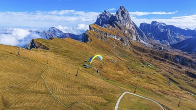 Paraglider over alpine meadows, in the background the peaks Sas Rigais and Furchetta of the Odle