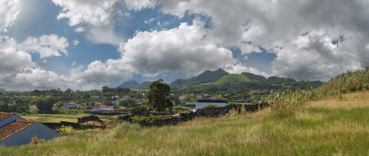 A peaceful rural landscape with houses, hills and volcanic mountains under a partly clear sky,