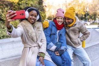 Three young multi ethnic friends are taking a selfie in a winter city, smiling and enjoying their