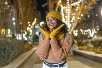 Smiling young woman wearing yellow woolen hat and gloves enjoying christmas lights in a city at