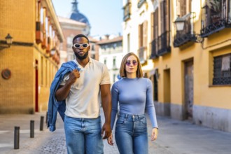 Frontal view of a stylish multiracial couple walking together with cool attitude along street