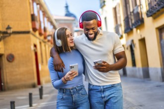 Multi-ethnic lovers embraced walking in the city using mobile phone and headphones