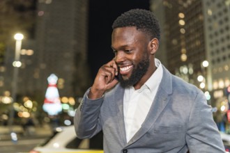 Young businessman smiling and chatting on a mobile phone while enjoying the vibrant city nightlife,