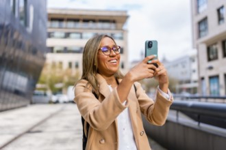 Happy latin woman visiting a city taking photos with a mobile phone