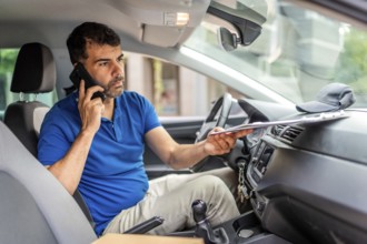 Mature caucasian male delivery person talking to the mobile phone sitting inside a van