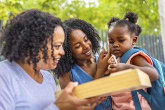 Cute african girl holding toys in arms of her mother next to her grandmother in a park