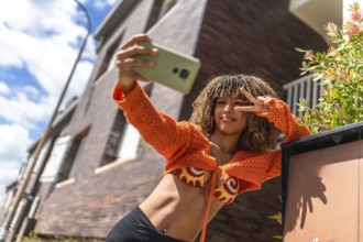 Latin student taking selfie gesturing success outside the house leaning in the entrance under the