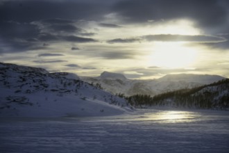View of snow-covered mountains and a frozen fjord during a dramatic sunrise, Norway, Europe