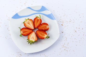 Aerial view of cut strawberries on a white plate with a white background with brown sugar