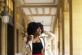 Elegant african businesswoman walking with a take away coffee next to a beauty modern building