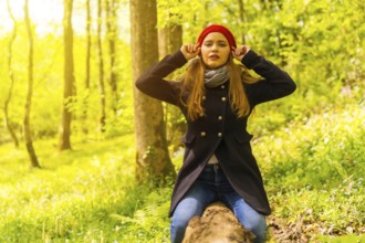 Beautiful woman with a black jacket and a red hat enjoying in an autumn park, sitting on a tree