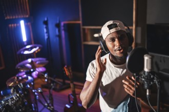 Young man recording vocals using a professional microphone and headphones in a music studio